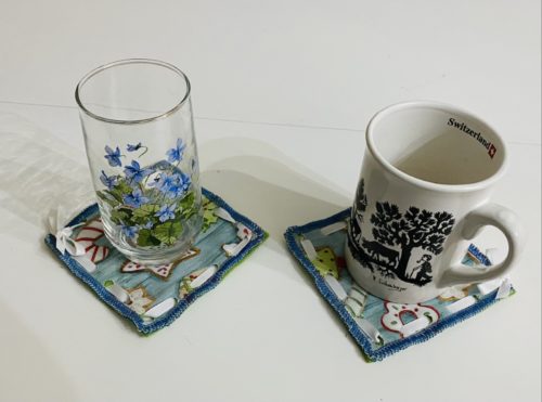 No sew coasters with light blue background and white, red, green iced Christmas Cookie pattern with two cups on top of coasters