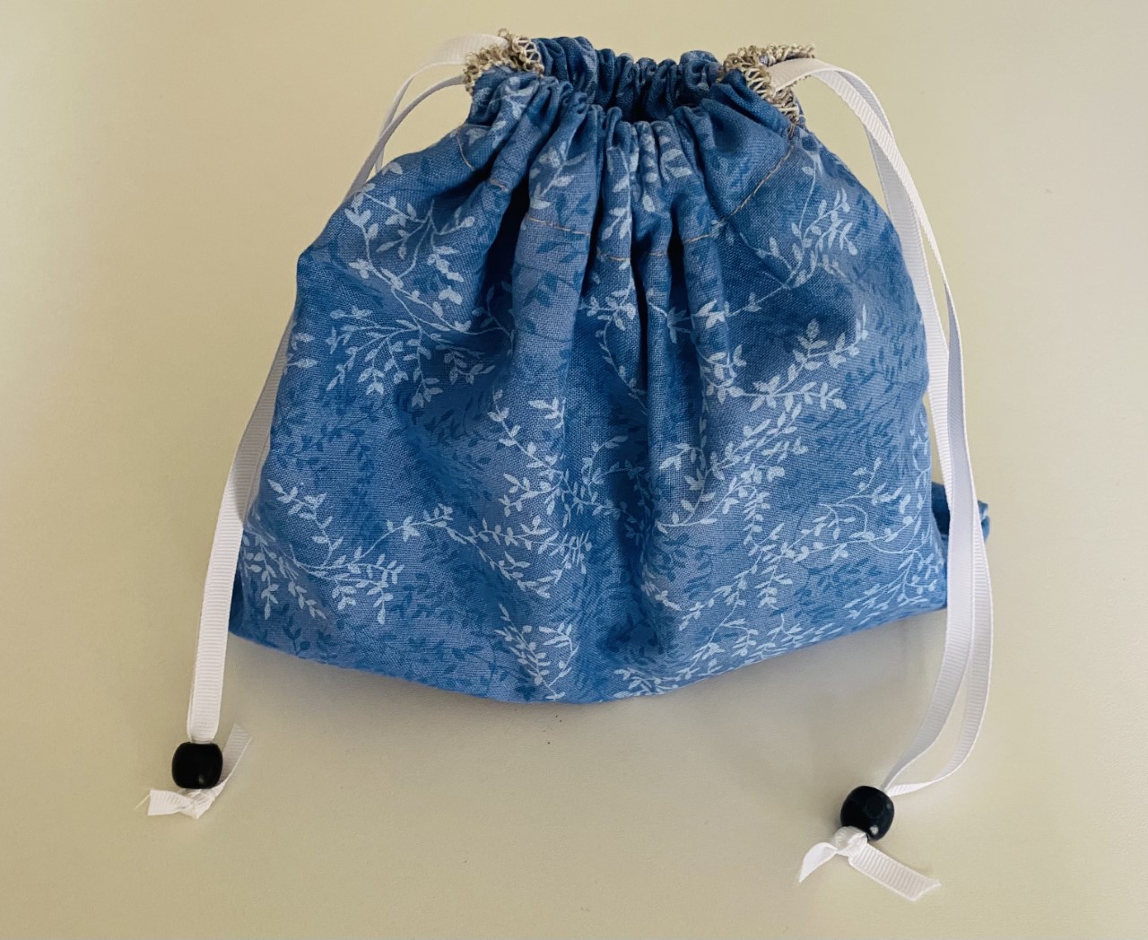 Ten inch drawstring bag with blue and white leaf pattern and small bead accents on white ribbon drawstrings