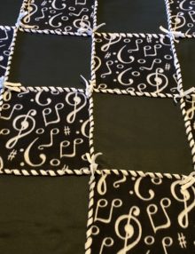 Fleece no sew 48 inch patchwork blanket with eight solid black fleece squares, alternated with eight black squares with white musical notes, woven together with white fleece ribbon