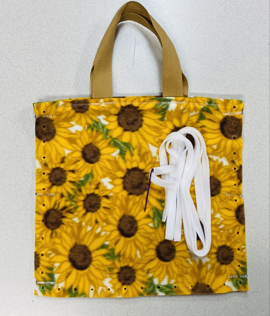 13" fleece tote bag in yellow, brown, and white with sunflowers and green leaves, tan tote straps, and white fleece ribbon to lace with plastic needle