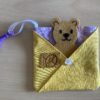 Pet in a Pocket Pouch - a light purple butterfly pocket with yellow and white floral pouch to carry a felt and faux suede teddy bear. Pouch pocket has a white floral button on center of pouch and a ribbon with hook in top left corner for attaching to loops.