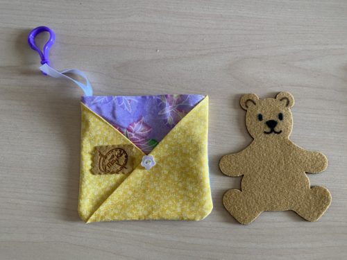 Pet in pocket pouch teddy bear beside pocket pouch in purple butterfly and yellow floral fabric.