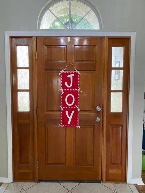 Red and White JOY Wall Hanging 30 inches by 10 inches with large white lettering and white running stitches with white ribbon