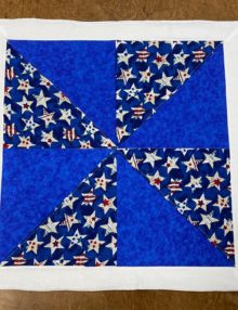23 inch fourth of July pinwheel quilt block table topper or wall hanging with four mottled blue 10-inch squares and four half-square triangles in a red, white, and blue star pattern, sewn onto alternating corners to create a pinwheel design.