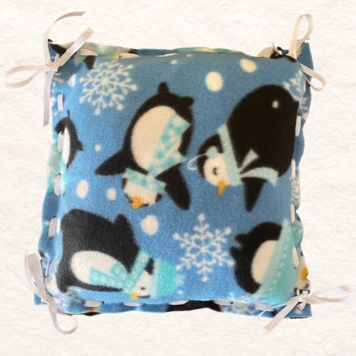 Penguin Pillow with light blue background, white snowflakes, black and white penguins with light blue scarves, and laced with white grosgrain ribbon