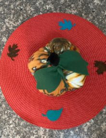 Top down photo of Fleece Pumpkin stuffed with polyfill and adorned with green leaves and black stem on top - about 8 inches around and five inches tall. The pumpkin is set on top of an orange 15" placemat decorated with felt fall leaves.