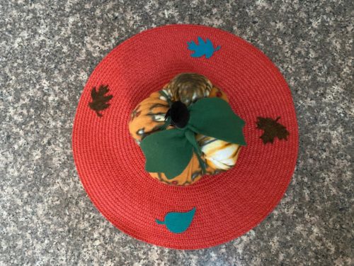 Top down photo of Fleece Pumpkin stuffed with polyfill and adorned with green leaves and black stem on top - about 8 inches around and five inches tall. The pumpkin is set on top of an orange 15" placemat decorated with felt fall leaves.