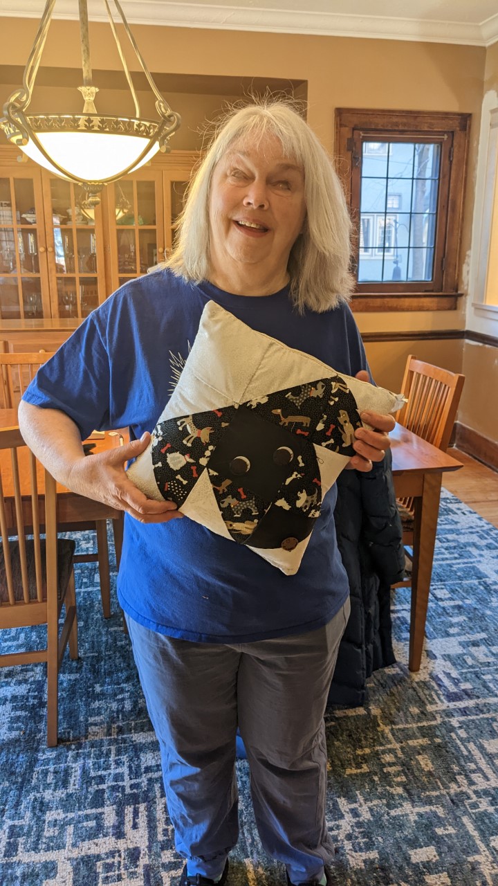 Merrilee Hill Kennedy holding her nine patch puppy dog face pillow she completed!